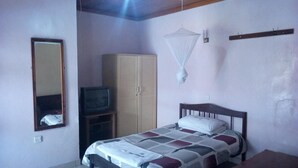 A bedroom with a bed, a wardrobe, a television on a stand, a bedside table, and a hanging mosquito net. - Mocharo Hotel (Isiolo)