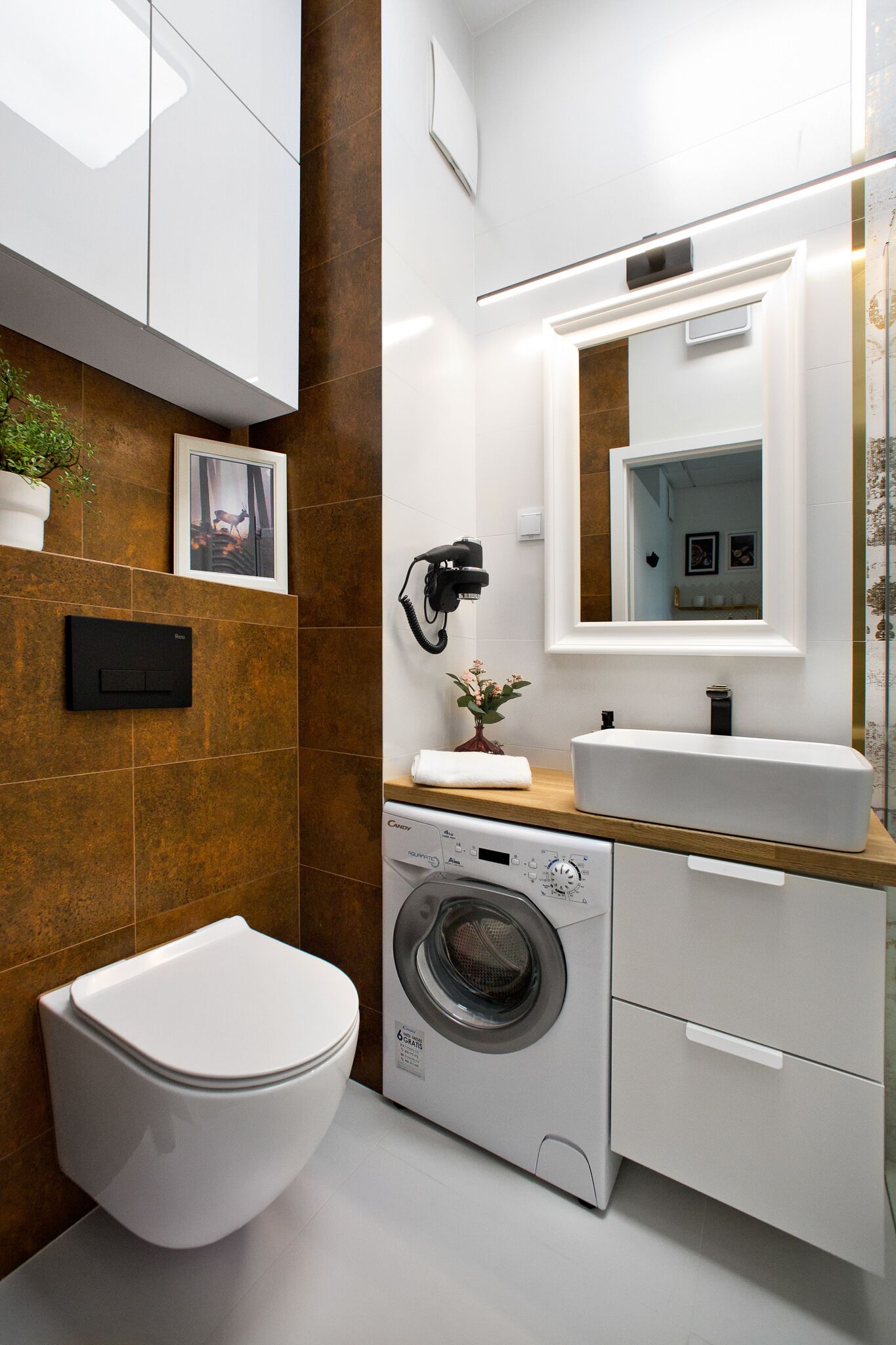 Een moderne badkamer met een wit toilet, een ingebouwde wasmachine, een wastafel en een spiegel.