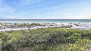 A beach with a flag, umbrellas, and sparse vegetation. - Stylish Beachfront Condo (Watersound)