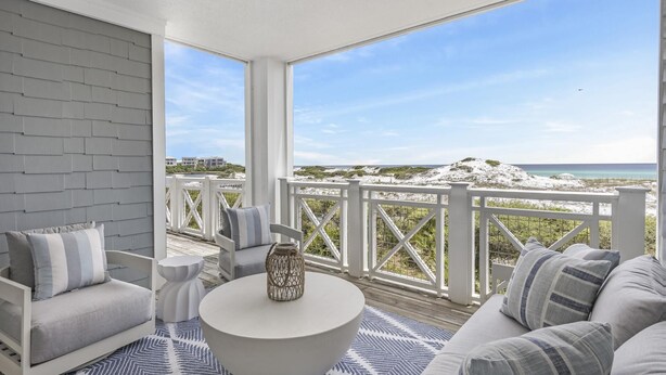A spacious balcony with a view of the beach and ocean, furnished with a sofa, chairs, and a coffee table. - Stylish Beachfront Condo (Watersound)