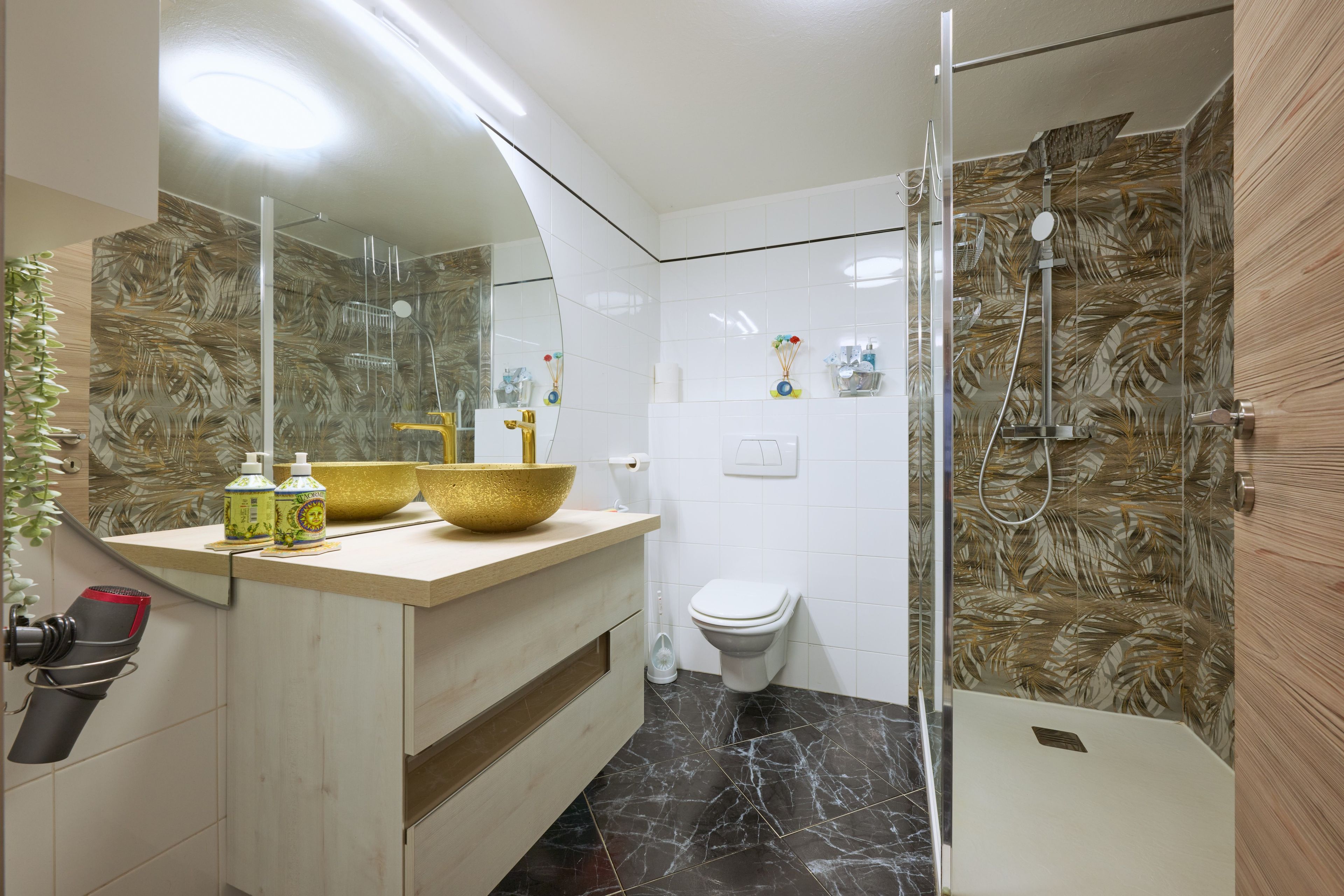 Ein Badezimmer mit einem großen Spiegel, einem goldenen Waschbecken, einer Toilette und einer Duschkabine.