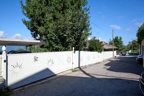 Une rue résidentielle bordée d’une clôture blanche, avec un grand arbre et des voitures garées.