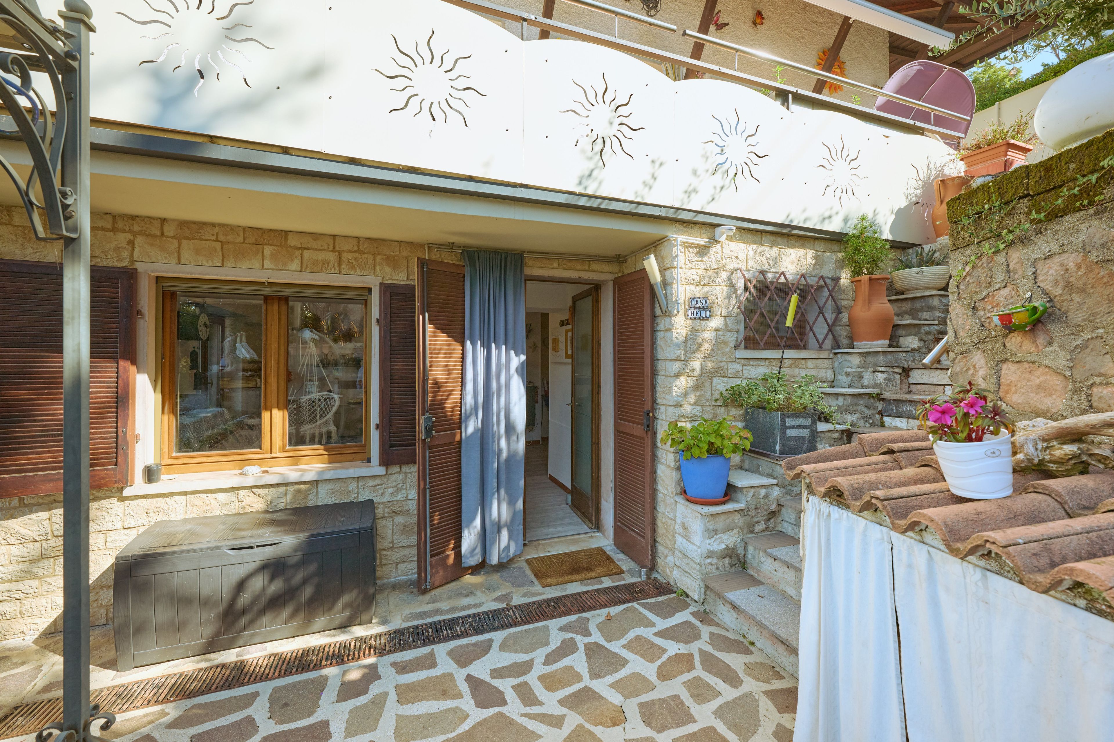 Ein Gebäude aus Stein mit einer gefliesten Terrasse, einer Holztür und einem Fenster mit Fensterläden.