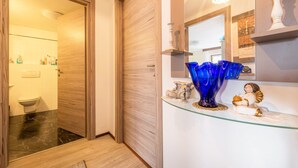 Une salle de bain avec une porte en bois, une cabine de douche en verre et un meuble-lavabo agrémenté d’un miroir et d’objets décoratifs.
