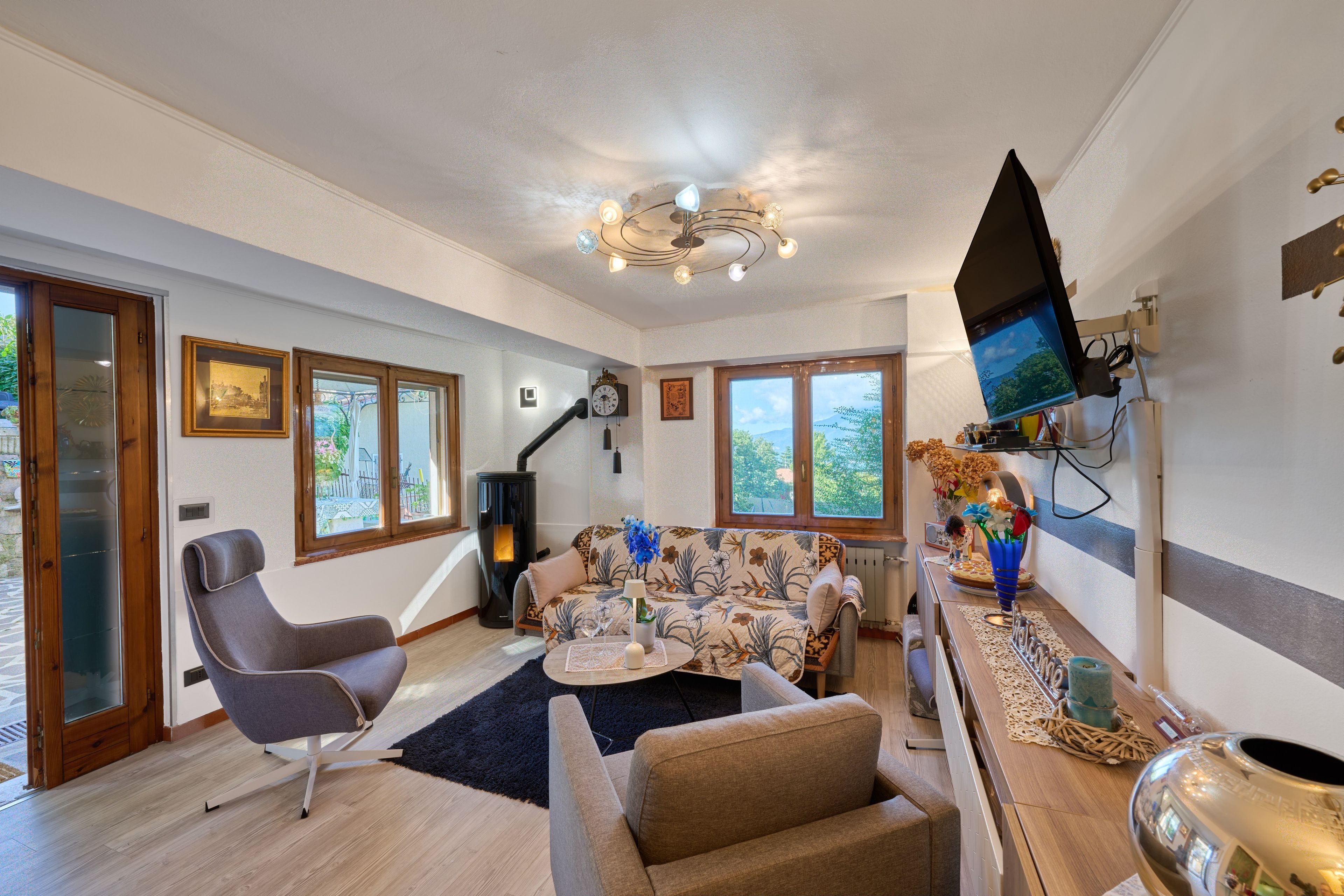 A spacious living area with a sofa, armchair, and a flat-screen TV mounted on the wall.