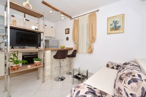 A compact living space with a kitchenette, a dining area with two bar stools, a bed with floral bedding, and a painting on the wall.