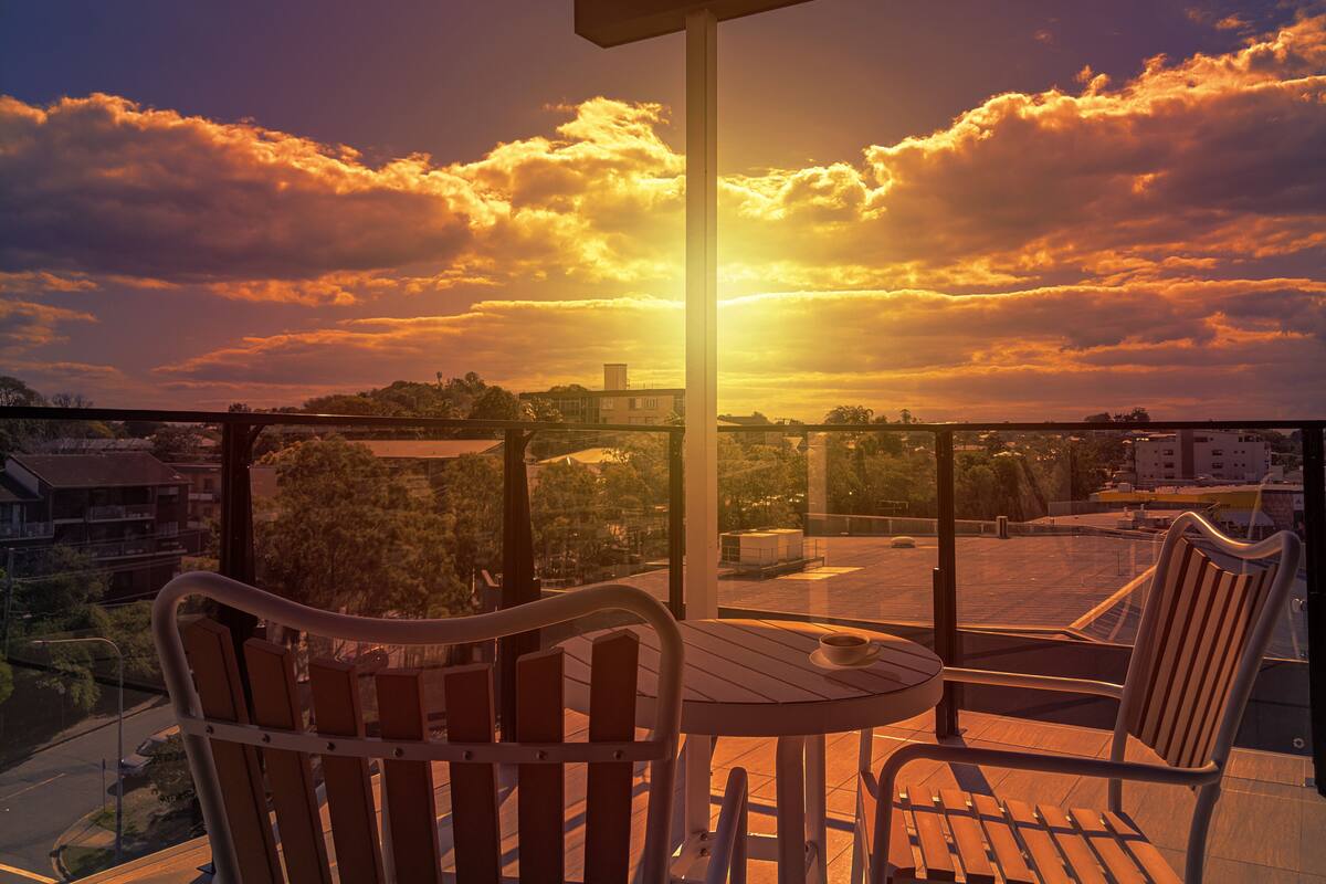 Un balcón con mesa y sillas, con vista a un paisaje urbano al atardecer.