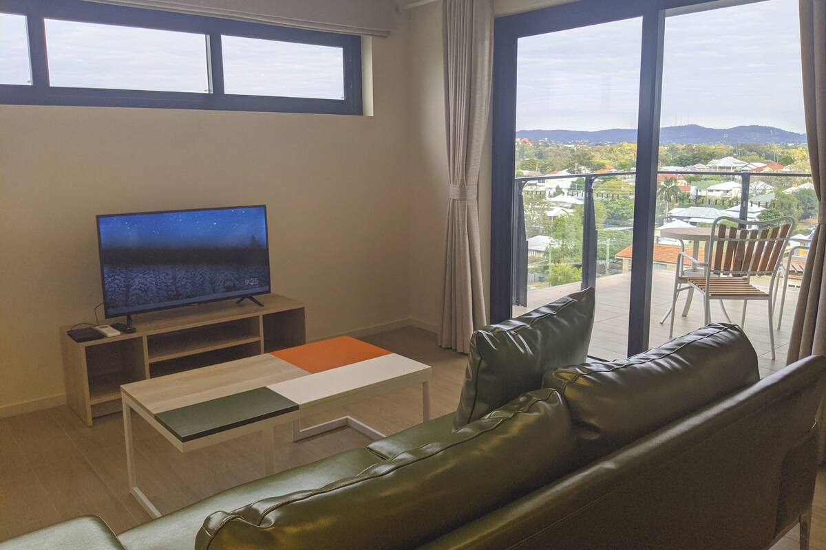 Una sala de estar moderna con un televisor de pantalla plana, un sofá, una mesa de centro y un balcón con vistas a la ciudad.
