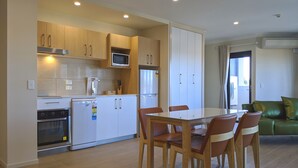 Cocina moderna con armarios blancos, microondas y refrigerador. Hay una mesa de comedor con sillas y un sofá verde en la sala de estar.