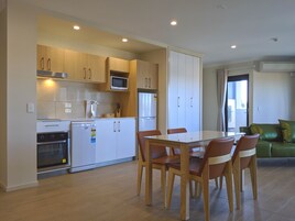 A modern kitchen with white cabinets, a microwave, and a refrigerator. There is a dining table with chairs and a green sofa in the living area.