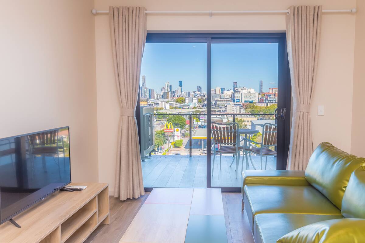 Un salón moderno con televisor de pantalla plana, un sofá y un balcón con vistas a la ciudad.