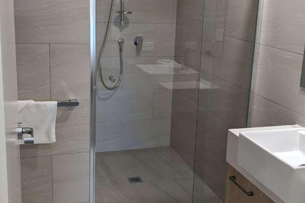 Un baño moderno con cabina de ducha de vidrio, un lavamanos blanco y un perchero para toallas.