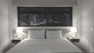 A hotel room with a large bed, two bedside tables with lamps, and a view of a cityscape at night.