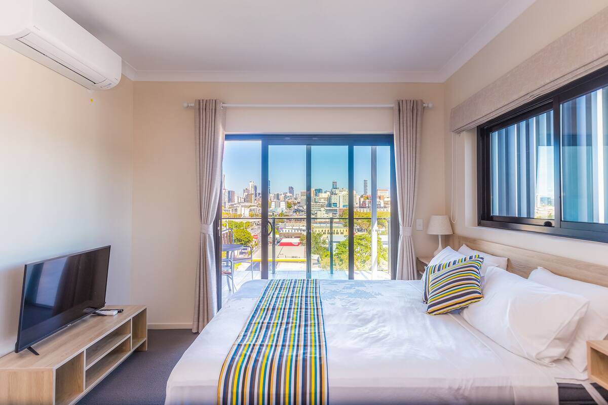 Habitación de hotel con una cama grande, televisión y vista a la ciudad por la ventana.