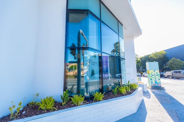 A modern building with large glass windows, a white exterior, and a landscaped area with plants. - The Windsor Apartments and Hotel Brisbane (Windsor)
