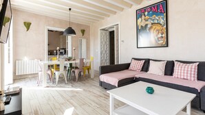 A living room with a sofa, a dining table with chairs, a kitchen area, and a poster on the wall. - Rustic Apartment "Casa Bugambilla" in Very Central Location with Balcony & Wi-Fi (Cadiz)