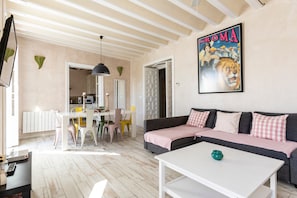 Un salon avec un canapé, une table à manger avec des chaises, un coin cuisine et une affiche accrochée au mur.