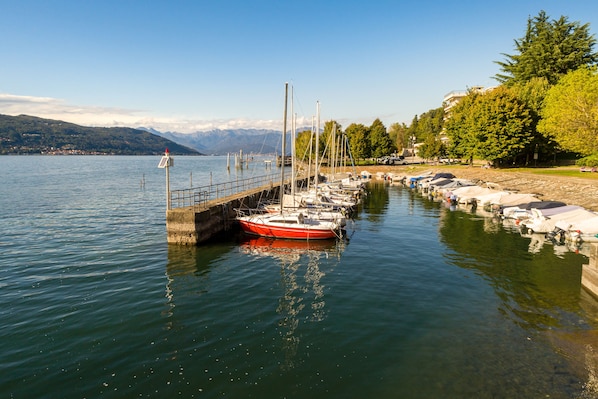 A calm lake with boats docked at a pier, surrounded by trees and mountains in the background. - Casa Al Caprifoglio 600 Mt From Beach (Ispra)