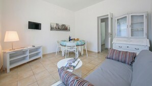 A living room with a sofa, a TV, a dining table with chairs, a cabinet, and a lamp. - Casa Al Caprifoglio 600 Mt From Beach (Ispra)