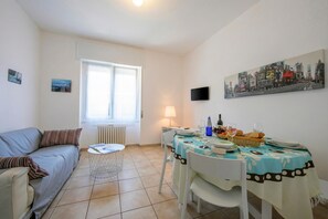 A living room with a sofa, a dining table with chairs, a lamp, and a painting on the wall. - Casa Al Caprifoglio 600 Mt From Beach (Ispra)