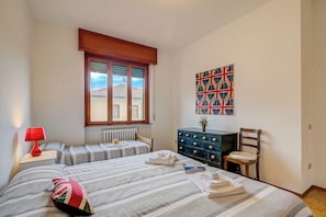 A bedroom with two beds, a dresser, a chair, a red lamp, and a window with blinds. - Connie's apartment Extra Pet Friendly (Monvalle)