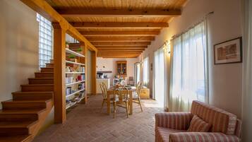 Un'ampia zona giorno con una scala in legno, un tavolo da pranzo con sedie, un divano e una libreria.