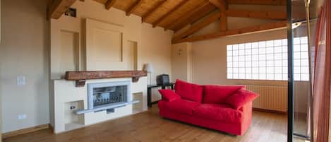 A room with a wooden ceiling, a fireplace, a red sofa, and a large window.