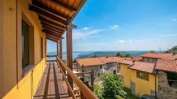 A balcony with a wooden floor and railing, overlooking a village with red-tiled roofs and a clear blue sky.