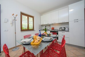 A modern kitchen with white cabinets, a dining table set with plates, a basket of bread, and red chairs.