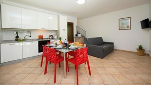 Una cocina moderna con armarios blancos, una mesa de comedor con sillas rojas, un sofá gris y una pequeña planta en el suelo.
