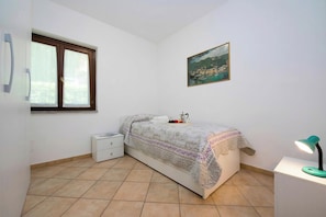 Une chambre à coucher avec un lit, une table de chevet, un bureau avec une lampe, une fenêtre et un tableau au mur.