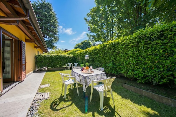 A patio with a table and chairs, surrounded by greenery and a building with a yellow facade.