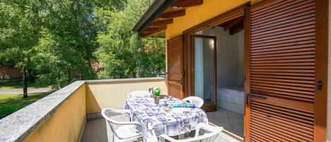 A balcony with a table and chairs, a wooden door, and a view of trees.