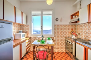 Una cocina con una mesa de comedor, sillas, refrigerador, microondas, estufa y ventana con vistas.