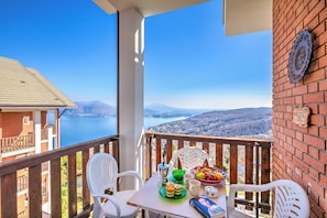 Un balcón con una mesa dispuesta para dos personas, vista a un lago y una pared de ladrillo con un plato decorativo.