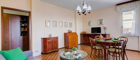 Una sala de estar con un sofá, una mesa de comedor con sillas, un televisor y una estantería.