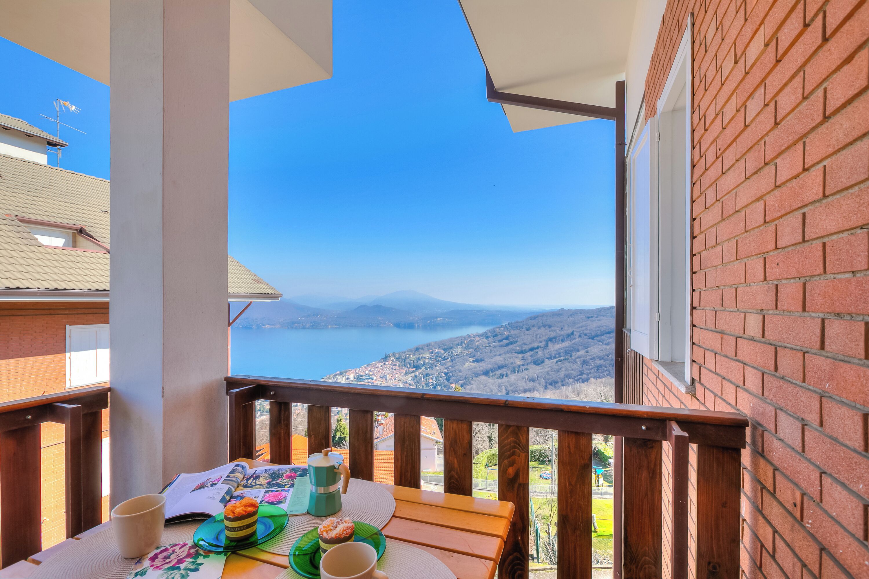 Ein Balkon mit gedecktem Tisch für das Frühstück, mit Blick auf eine malerische Seen- und Berglandschaft.