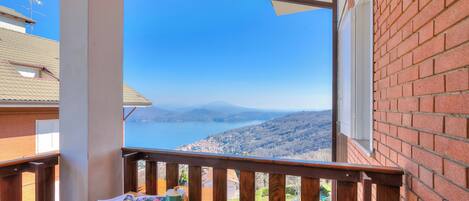 A balcony with a table set for breakfast, overlooking a scenic view of a lake and mountains.
