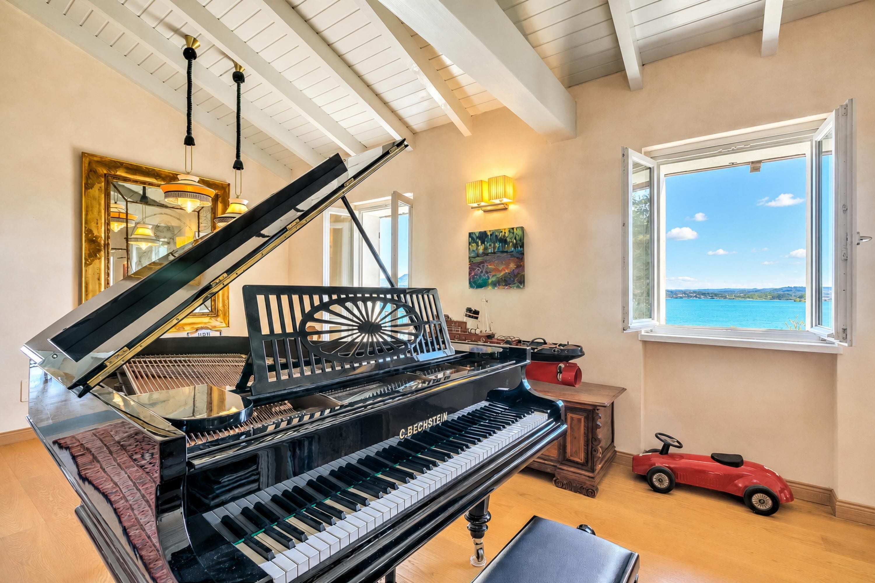 Un piano à queue dans une pièce dotée d’une grande fenêtre, d’un tableau et d’une voiture jouet.