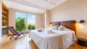 Ein Schlafzimmer mit einem großen Bett, einem Holzstuhl, einem Bücherregal und Blick ins Grüne.