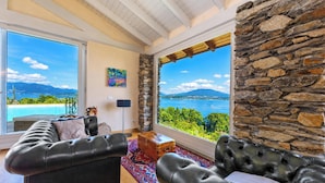 Ein geräumiges Wohnzimmer mit großem Fenster, das einen Blick auf Pool und Berge bietet, einer Steinwand und einem Ledersofa.