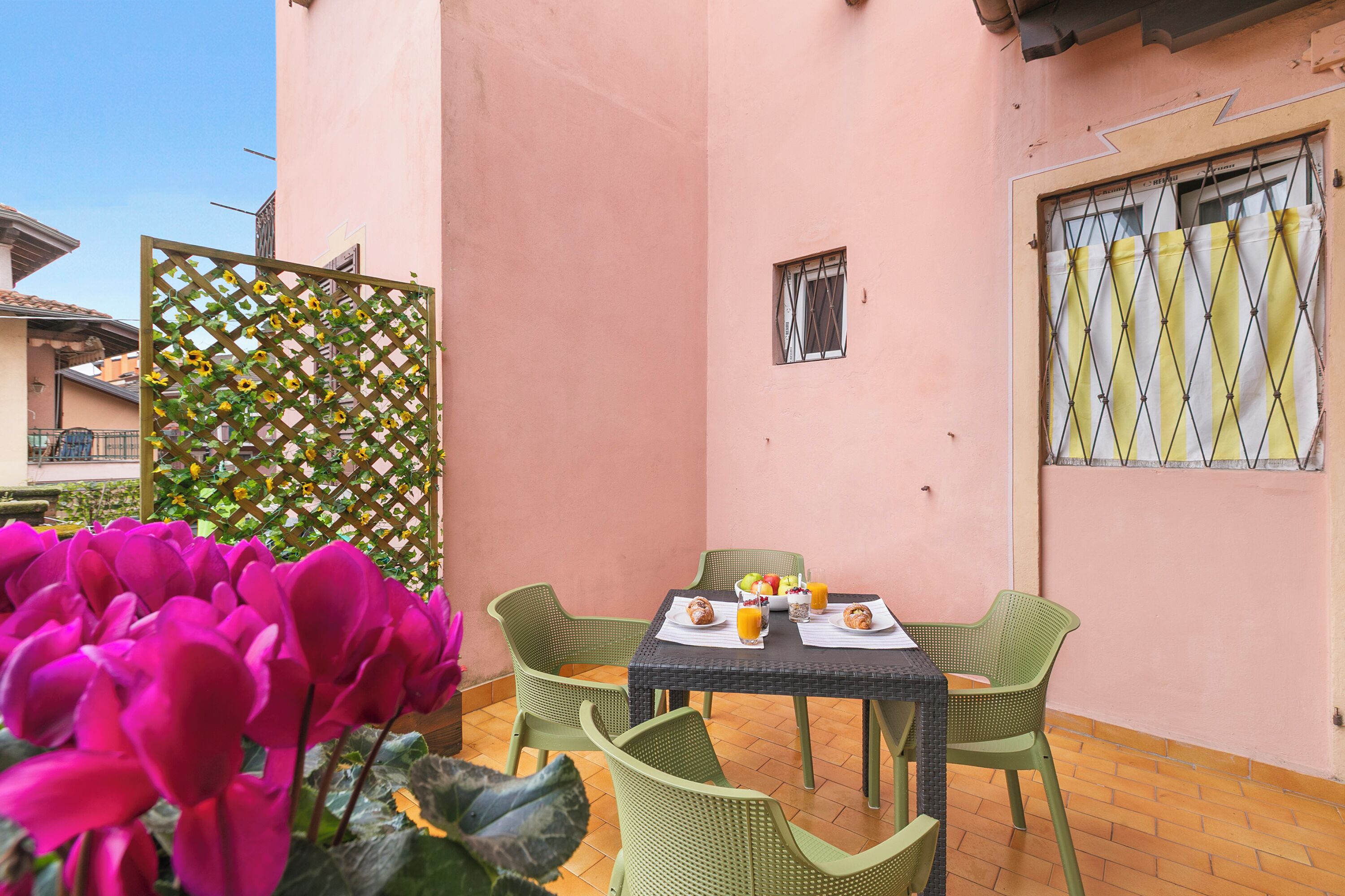 Un pequeño patio con una mesa preparada para dos, rodeado de sillas verdes.