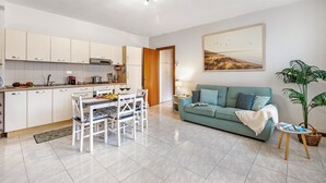 A modern kitchen with white cabinets, a dining table with chairs, a green sofa, and a large window. - Petalo Bianco 100m from lake (Baveno)
