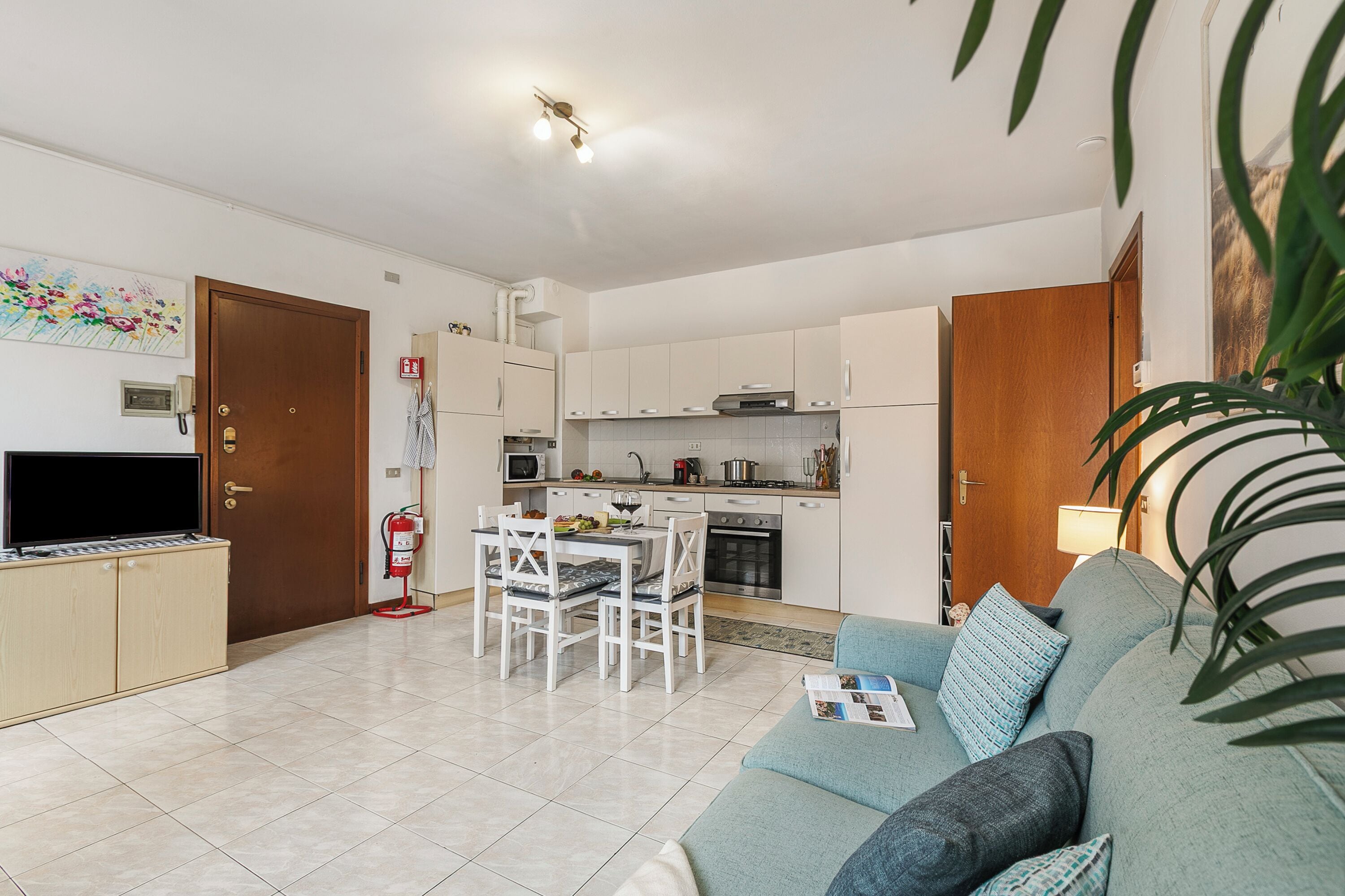 Ein modernes Wohnzimmer mit einer Couch, einem Esstisch mit Stühlen und einer Küchenzeile mit Schränken und Geräten.