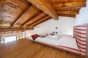 A bedroom with a sloped ceiling, wooden beams, a bed with a striped blanket, and a bedside table with a lamp. - Relax al Moro Apt with Pool (Leggiuno)
