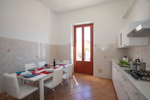 A kitchen with a dining area, white cabinets, a red door, and a view through the door.