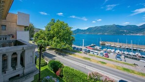 Uma estrada costeira com um porto de recreio, uma grande árvore e montanhas ao fundo.
