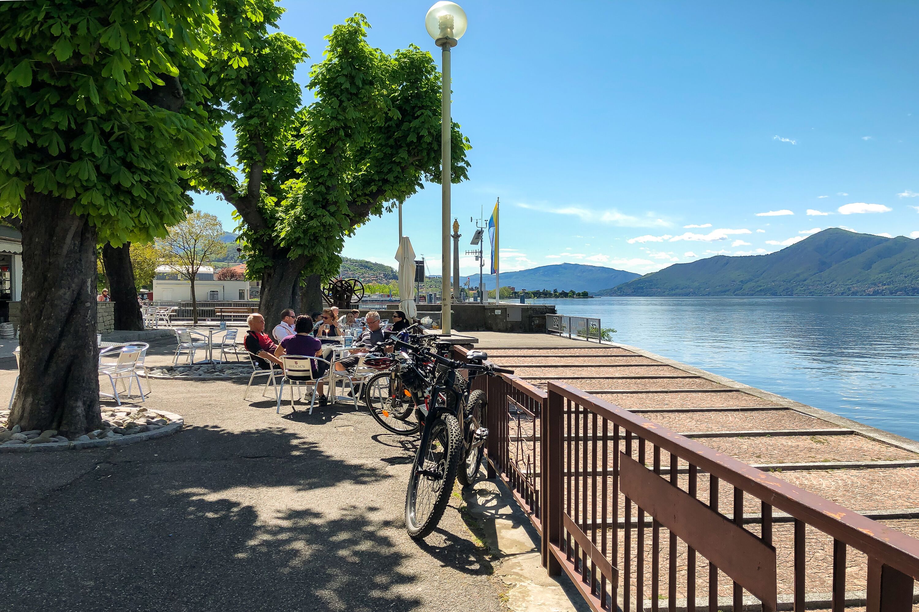 A lakeside café with outdoor seating, bicycles, and a view of the lake and mountains.