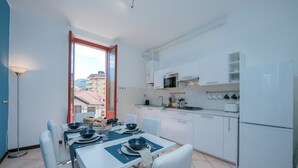 Cozinha moderna com armários brancos, micro-ondas e geladeira. Há uma área de jantar com mesa posta para quatro pessoas, incluindo tigelas, pratos e talheres.