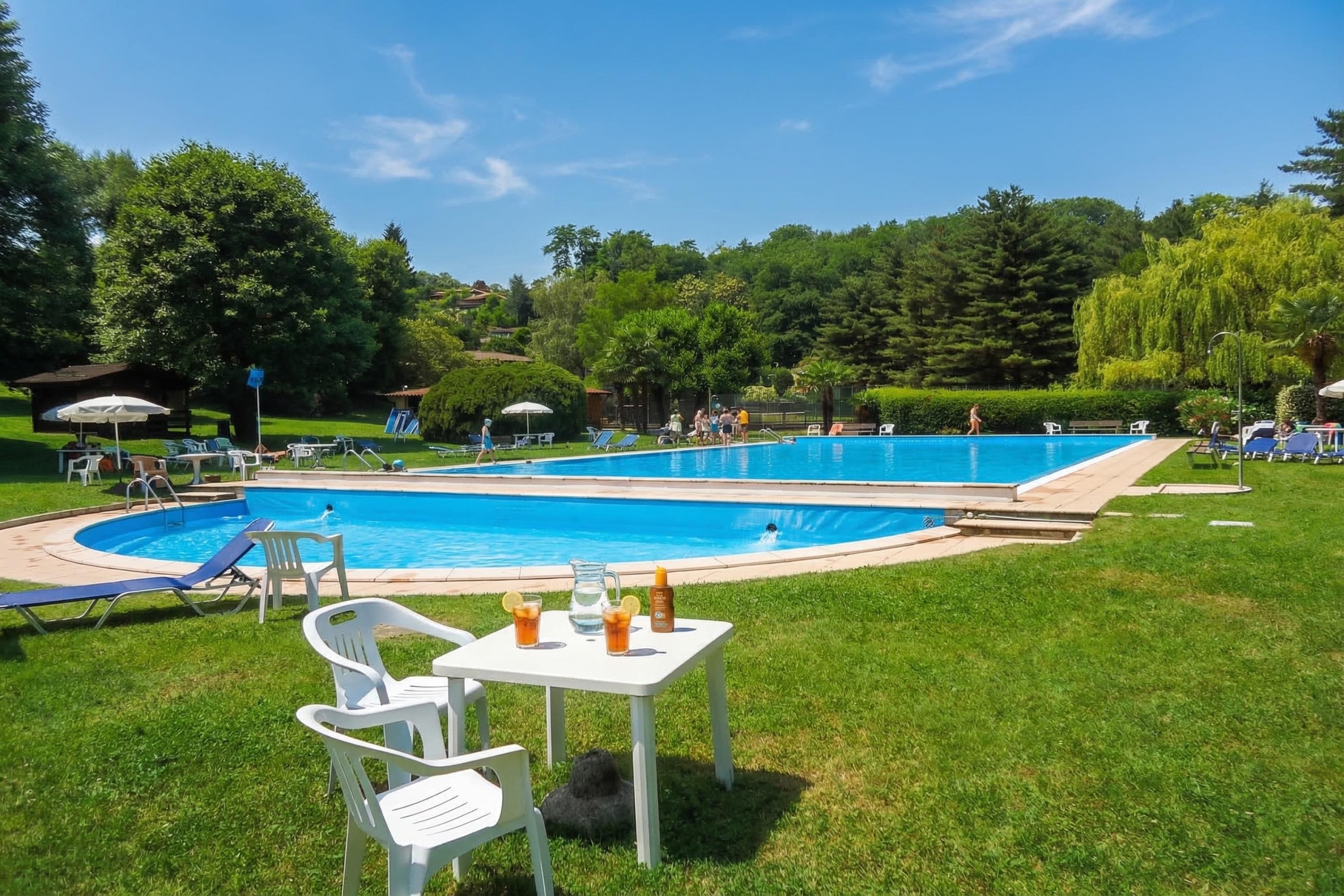 Ein Swimmingpool mit Liegestühlen und Tischen, umgeben von viel Grün.